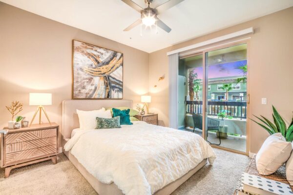 Bedroom with plush bed, bedside chests with lamps, framed art, and balcony door.