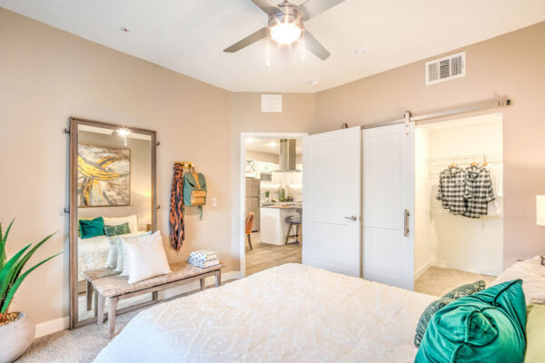 Bedroom with plush bed, bench with pillows, large mirror, and closet door.