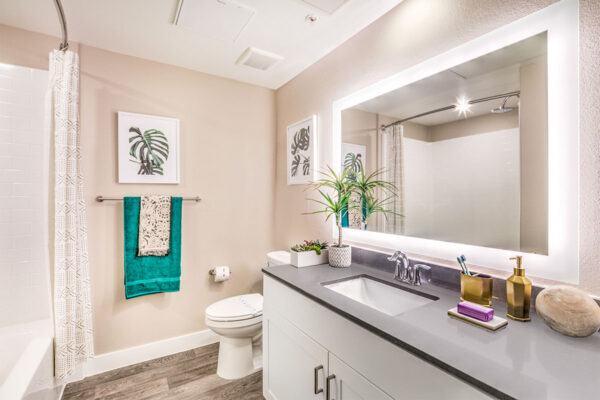 Bathroom with wood floor, white cabinets, lighted mirror, and tiled shower tub.