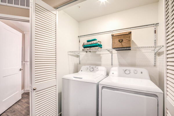 Laundry closet with washer, dryer, and shelf with storage and linens.