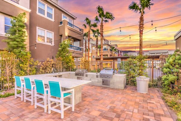 Outdoor BBQ area with built in grills, sink, dining surface, and palm trees.