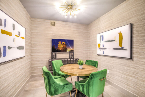 Business center with round table, green chairs, TV, and framed art.