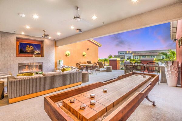 Indoor/outdoor lounge with fireplace, TV, plush couches, and shuffleboard table.