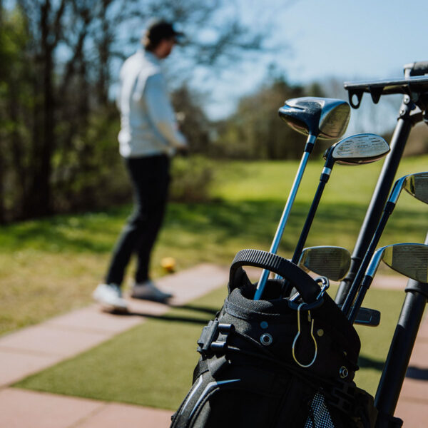 Person golfing with clubs in bag in bright sunshine.