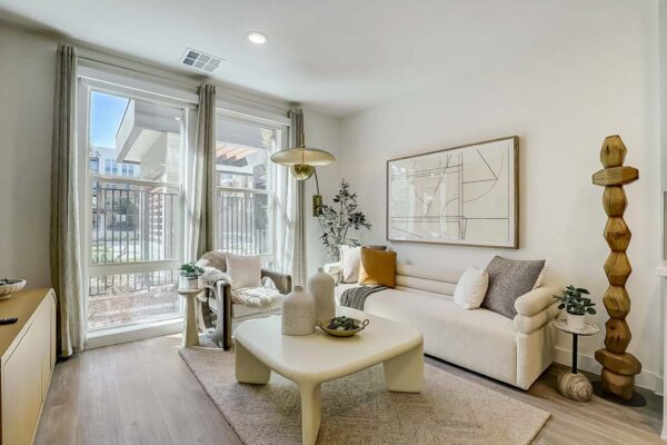 Aspire at Redwood apartment living room with plush couch, eclectic artwork, brass lamp, and balcony door.