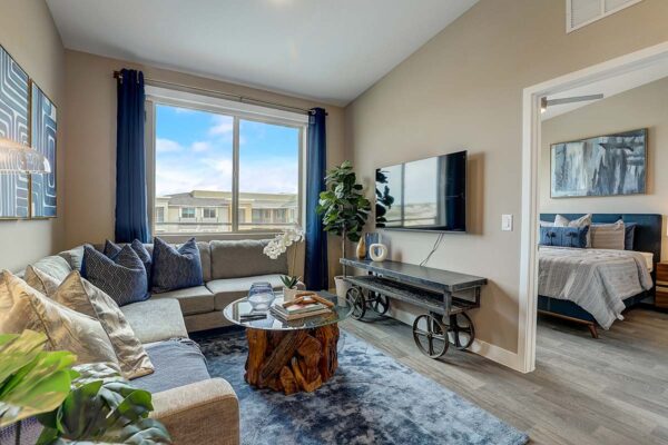 Aspire at Echelon apartment living room with wood style floor, plush sectional, wall mounted TV, and large window.