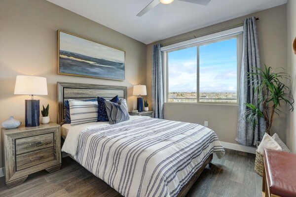 Aspire at Echelon apartment bedroom with wood style floor, plush bed with headboard, and large window.