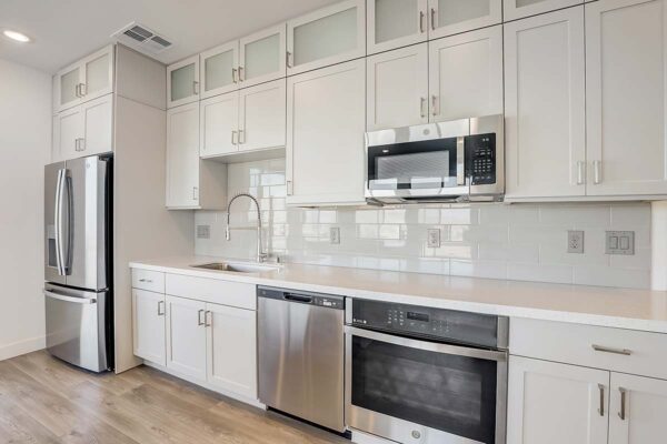 Aspire at Redwood apartment kitchen with wood style floor, white cabinets, light counters, and stainless steel appliances.