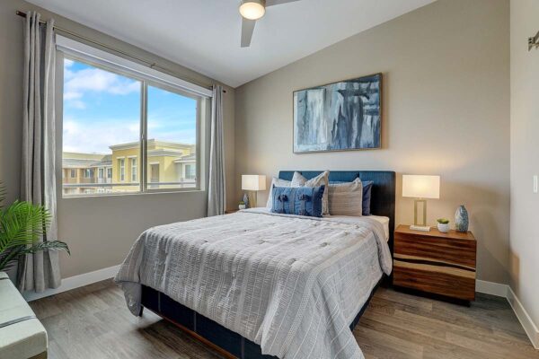 Aspire at Echelon apartment bedroom with wood style floor, plush bed with headboard, and large windows.
