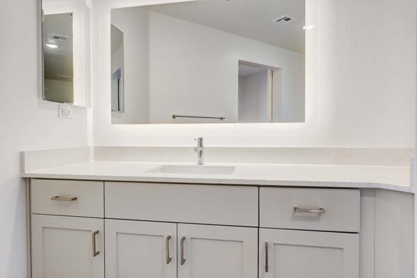 Aspire at Redwood apartment bathroom with white cabinets and counters and lighted mirror.