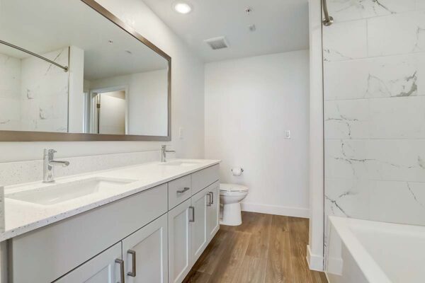 Aspire at Redwood apartment bathroom with wood style floor, white cabinets and counters, and framed mirror.
