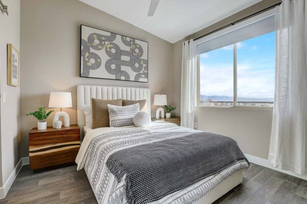 Aspire at Echelon apartment bedroom with wood style floor, plush bed with headboard, large artwork, and large window.