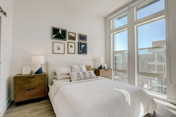 Aspire at Redwood apartment bedroom with wood style floor, plush bed with headboard, and large windows.