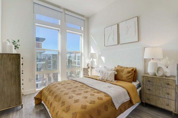 Aspire at Redwood apartment bedroom with wood style floor, plush bed with headboard, and large windows.