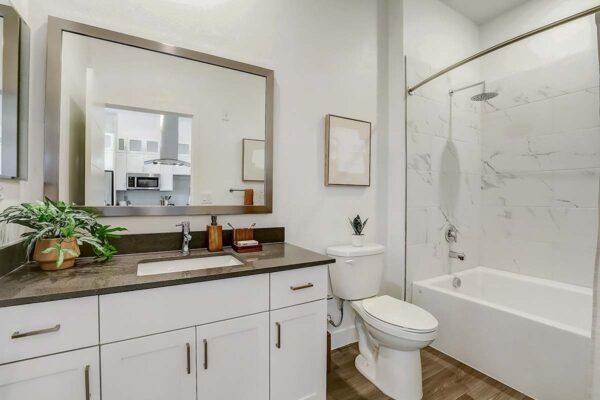 Aspire at Redwood apartment bathroom with wood style floor, white cabinets, framed mirror, and tiled shower tub.