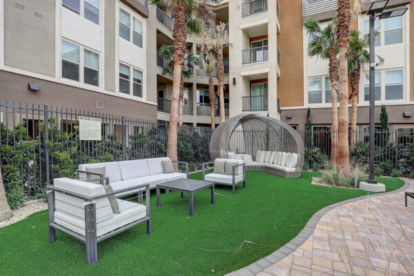 Aspire at Echelon apartments outdoor lounge with stone paver patio, turf lawn, plush seating, and palm trees.