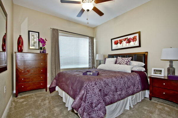 Bedroom with carpet, plush bed with headboard, bedside drawers with lamps, and wood dresser.