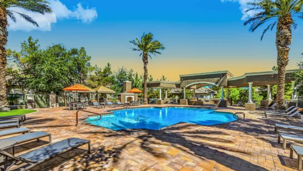 Pool area with stone paver patio, lounge chairs, gazebos, and BBQ grills.
