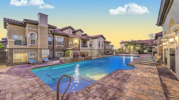Pool area with dining table, waterfall, and pool with lounge chairs.