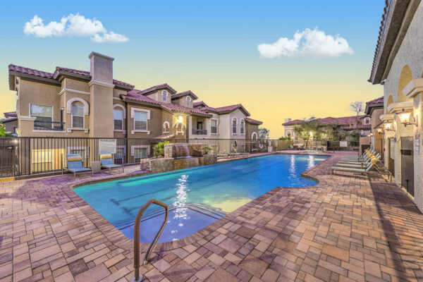 Pool area with dining table, waterfall, and pool with lounge chairs.