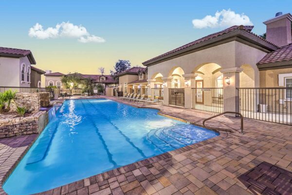 Pool area with stone paver patio, lounge chairs, and waterfall.