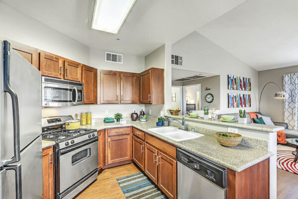 Kitchen with wood cabinets, stone counters, stainless steel appliances, and breakfast bar with stools.