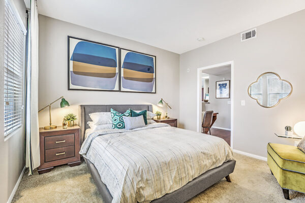 Bedroom with plush bed, bedside drawers with lamps, large framed artwork, and large windows.