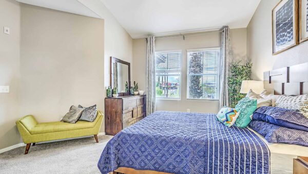 Bedroom with plush bed, daybed with pillows, dresser with mirror, and large windows.