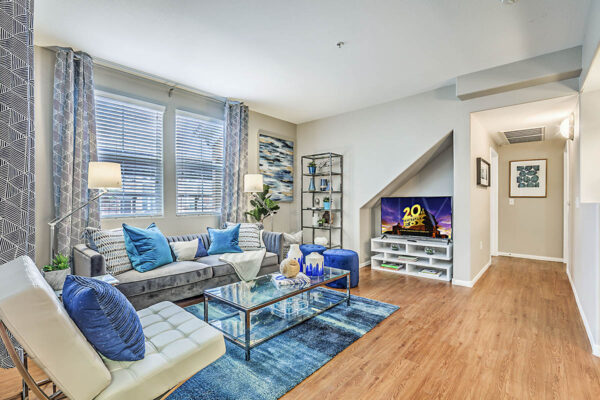 Living room with wood floor, plush seating, shelves with decor, and large windows.