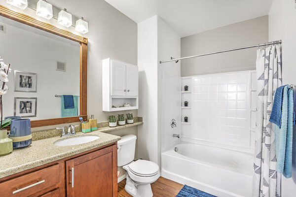 Bathroom with wood cabinets, stone counters, framed mirror, and tiled shower tub.