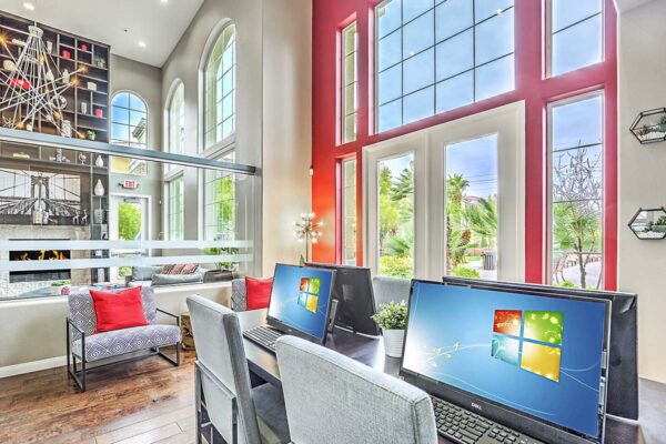 Business center with tables, computers, plush chairs, and two story windows.