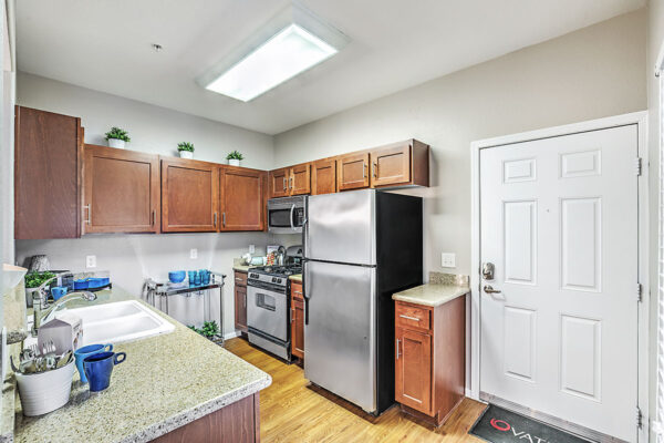 Kitchen with wood floor and cabinets, stone counters, and stainless steel appliances.
