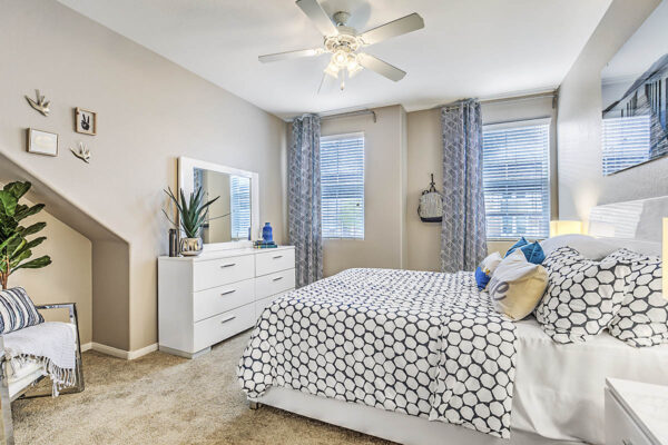 Bedroom with plush bed, large dresser with mirror, ceiling fan, and large windows.