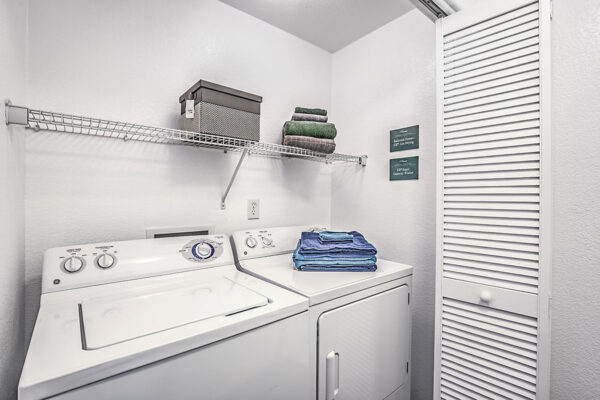 Laundry room with washer and dryer and shelves with towels and boxes.