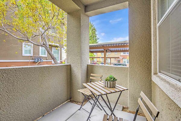 Patio with outdoor furniture and potted plant overlooking trees and parking area.