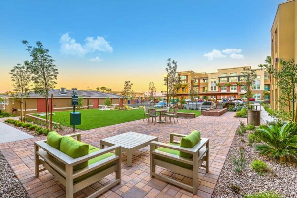 Outdoor lounge with stone paver patio, plush seats, dining table with chairs, and lush landscaping.