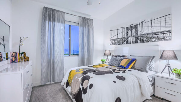 Bedroom with plush bed, bedside dressers with lamps, dresser with decor, and large window.