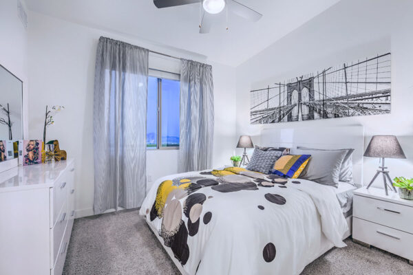 Bedroom with plush bed, bedside dressers with lamps, dresser with decor, and large window.