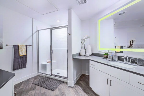 Bathroom with wood floor, white cabinets, lighted mirror, and glass wall shower.