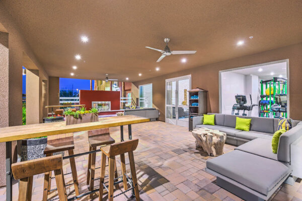 Outdoor patio with plush seating, tall tables with stools, ceiling fan, and outdoor fireplace.