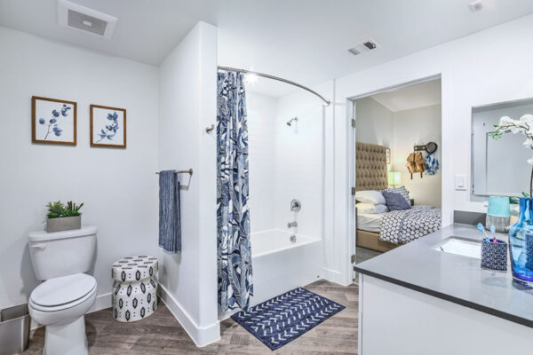 Bathroom with stone counters, medicine cabinet, tiled shower tub, and door to bedroom.