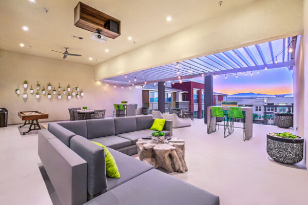 Rooftop patio with plush seating, dining tables with stools, projector TV, and shuffleboard table.