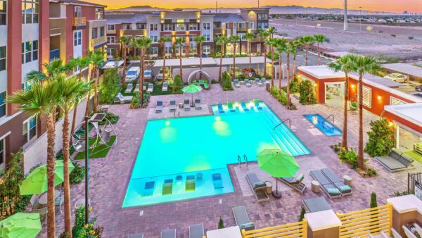 Overhead view of pool area with lounge chairs, umbrellas, stone paver patio, and lush landscaping.