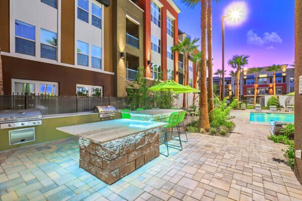 Outdoor lounge with built in BBQ grills, stone tables with chairs, and lush landscaping.