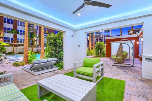 Outdoor lounge with ceiling fan, plush chairs, stone paver patio, and lush landscaping.