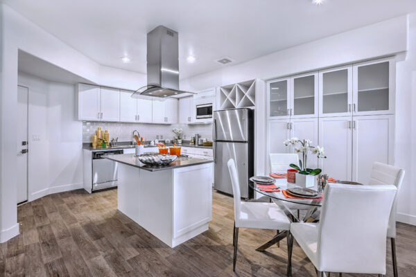 Kitchen with wood floor, white cabinets, stone counters, stainless steel appliances, and dining table with chairs.