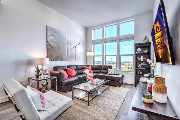Apartment living room with plush leather seating, shelves with decor, artwork, and large window.