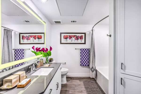 Bathroom with white cabinets, stone counter, lighted mirror, and tiled shower tub.
