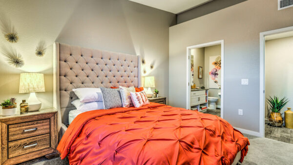 Bedroom with carpet, plush bed with headboard, drawers with lamps, and bathroom door.