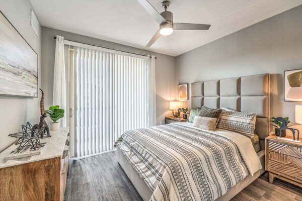 Bedroom with plush bed, bedside tables with lamps and decor, and sliding door to balcony.
